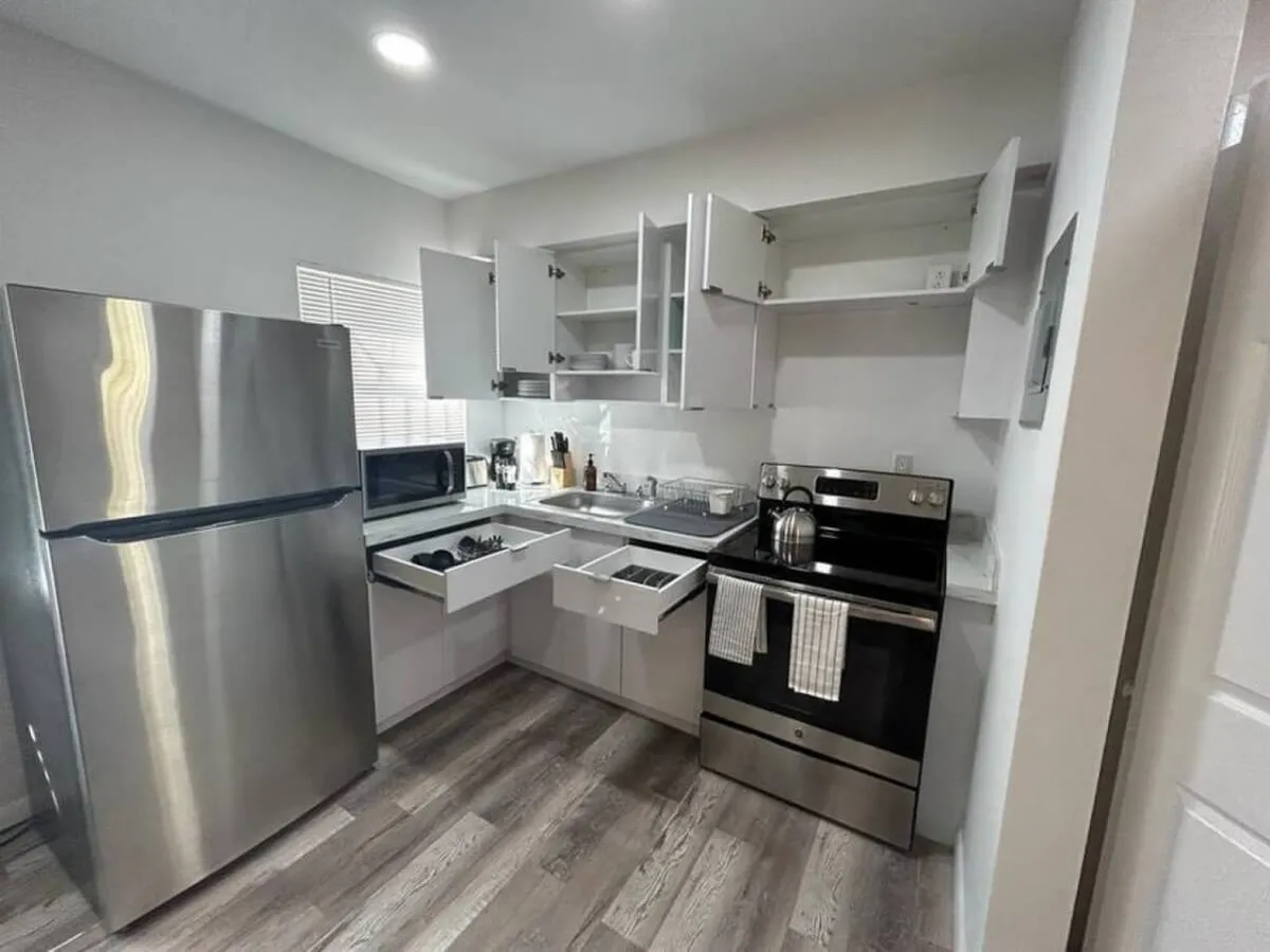 Featuring a stainless steel refrigerator and a sleek black stove, this kitchen view also captures open cabinets ready for easy access to utensils and cookware. The setup is practical yet stylish, reinforcing the user-friendly design of the space.