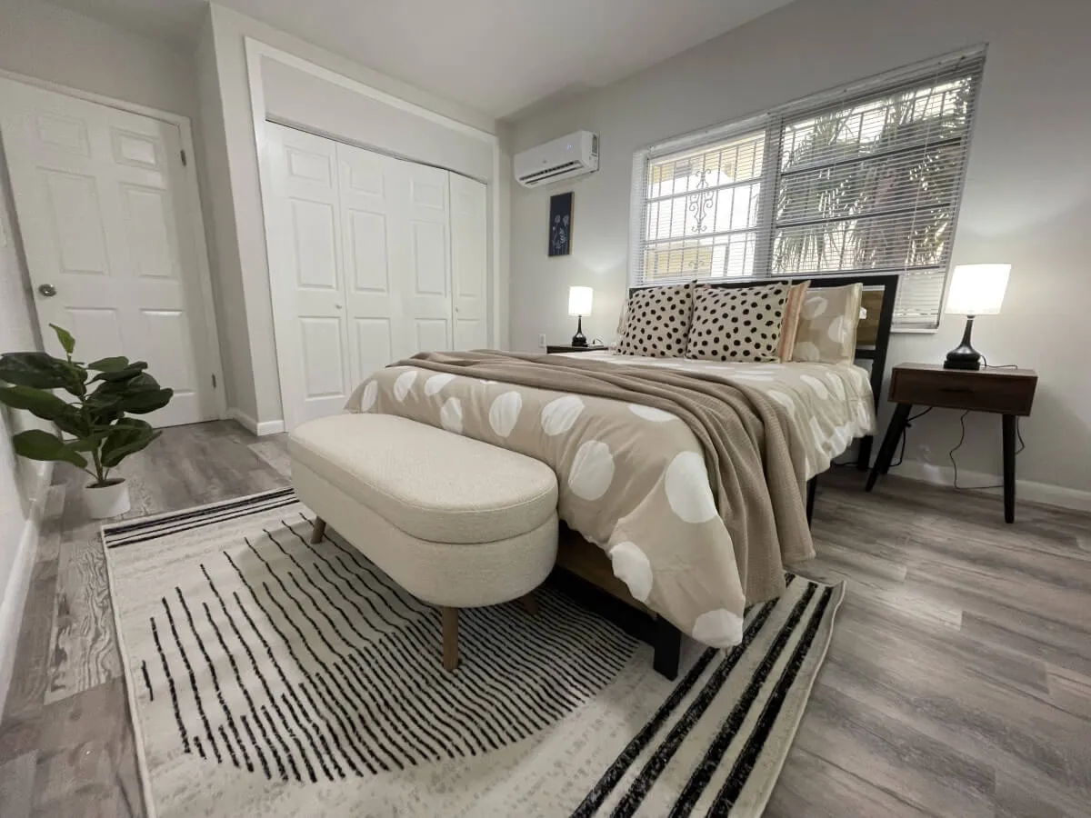 A cozy and serene bedroom scene featuring a queen bed with patterned bedding, flanked by nightstands with softly glowing lamps. A potted plant in the corner and a rug with bold patterns create a warm, inviting atmosphere ideal for downtime and relaxation.