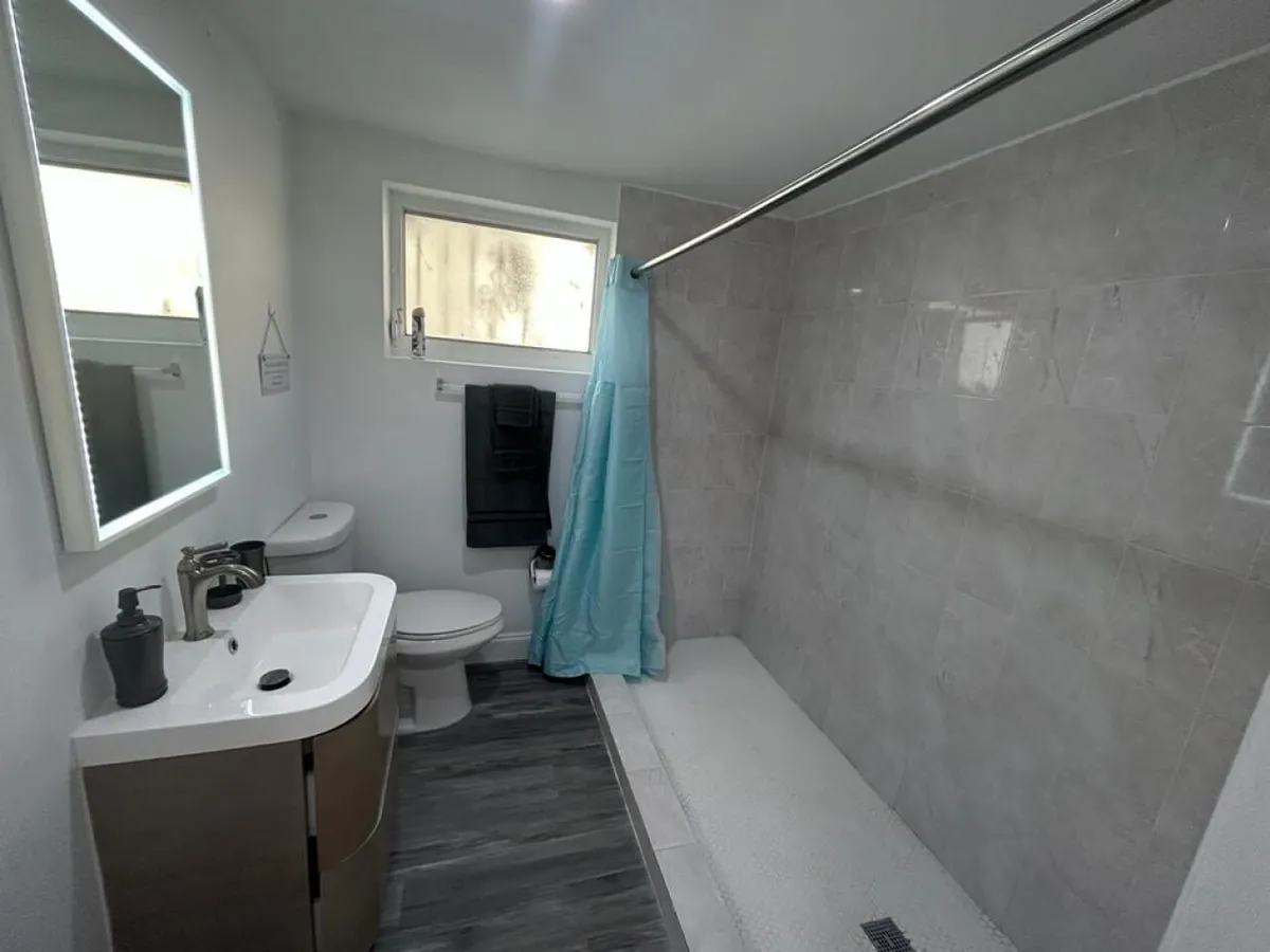 A spacious, inviting bathroom with a large mirror, modern vanity, glass-enclosed shower, and a toilet. The clean, tranquil design sets the scene for relaxing routines, whether prepping in the morning or unwinding at night.