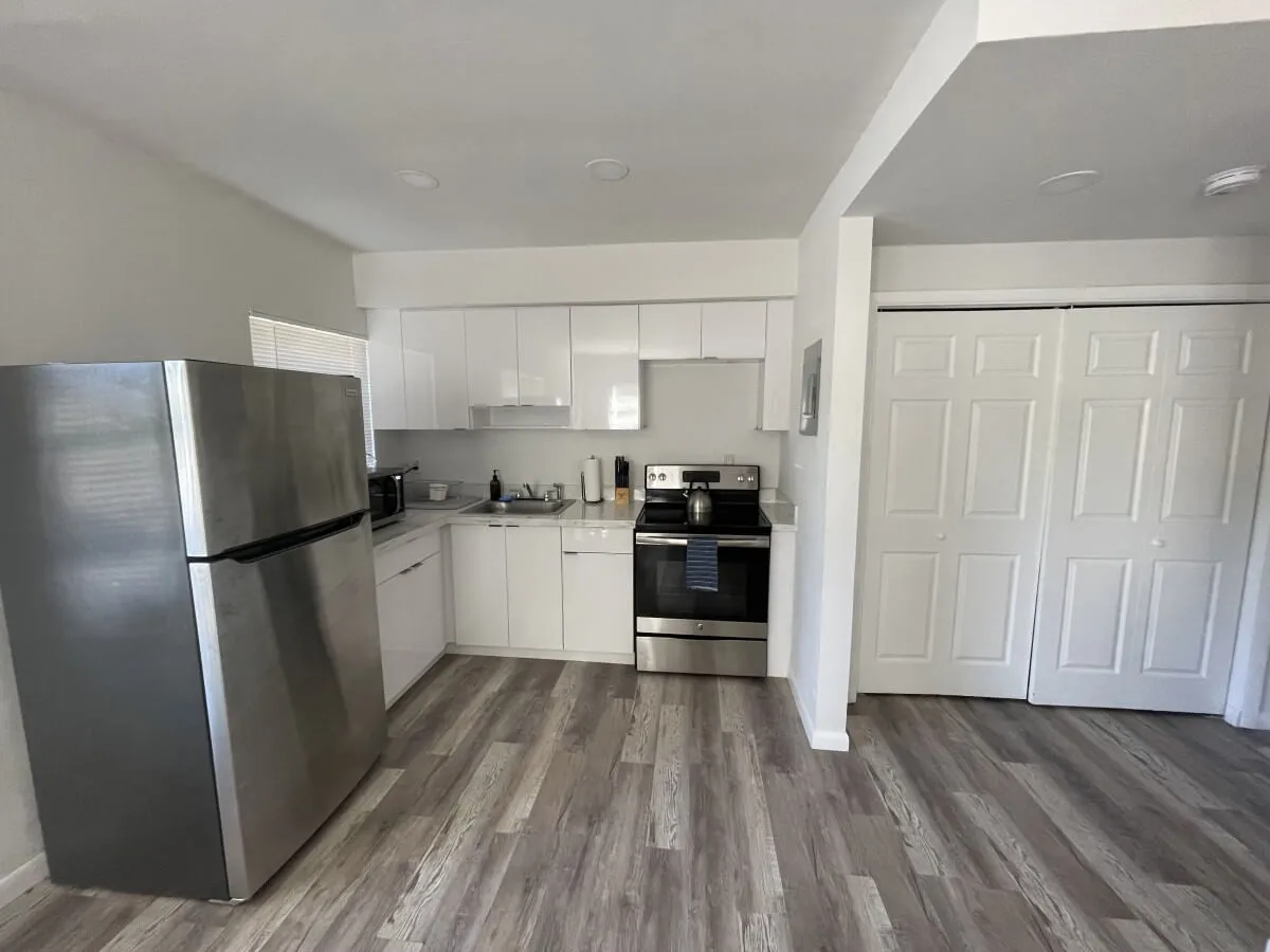 This image showcases a bright and modern kitchen space with stainless steel appliances, including a refrigerator and stove, complemented by fresh white cabinetry and warm wooden flooring. The room is well-lit and inviting, emphasizing a contemporary atmosphere ideal for both cooking and entertaining.